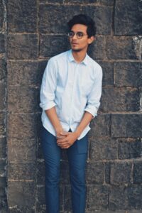 Stylish young man with eyeglasses posing against a brick wall outdoors.